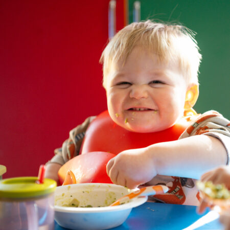 A child sitting in a high chair eating a bowl of food.